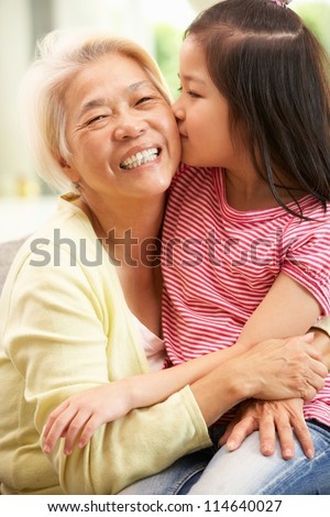 Chinese Grandmother And Granddaughter Relaxing On Sofa At Home