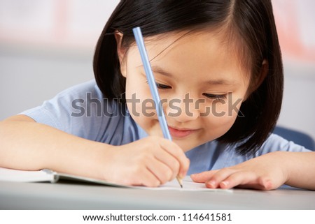 Female Student Working At Desk In Chinese School Classroom