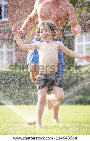 Father And Son Running Through Garden Sprinkler