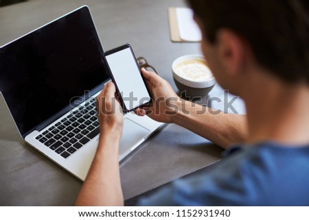 Young man using smartphone in a coffee shop, back view