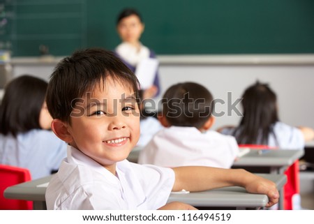 Portrait Of Male Pupil Working At Desk In Chinese School Classroom