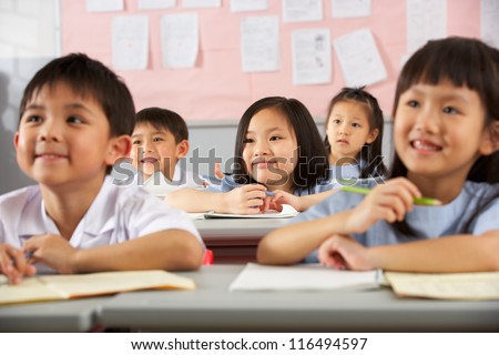 Group Of Students Working At Desks In Chinese School Classroom