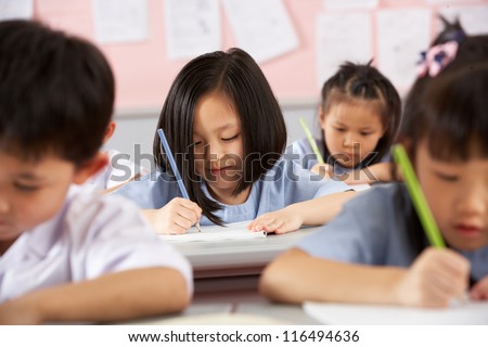 Group Of Students Working At Desks In Chinese School Classroom
