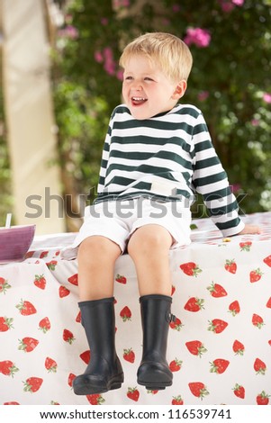Young Boy Wearing Wellington Boots Sitting On Table