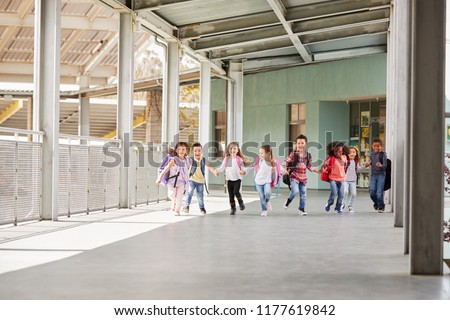 Primary school kids run holding hands in school corridor