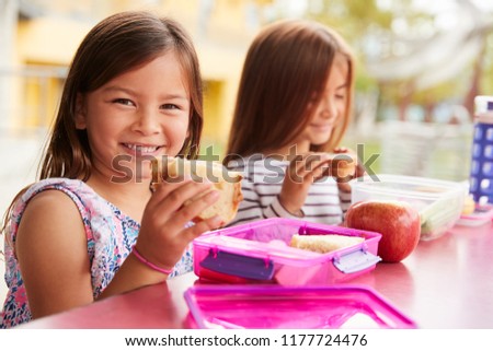 Young schoolgirls holding sandwiches at school lunch table