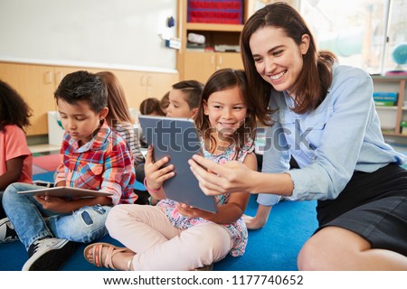 Teacher and girl in elementary class using tablet computers