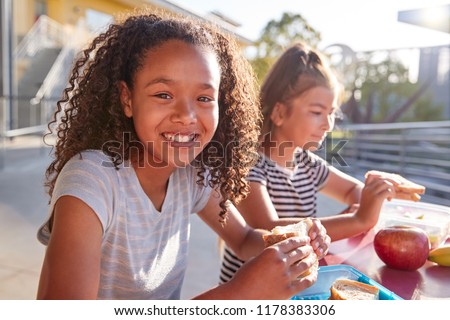 Girlfriends at school lunch table, one smiling to camera