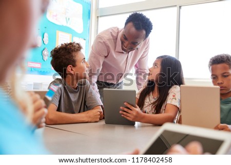 Teacher among kids with computers in elementary school class