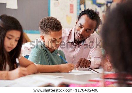 Male teacher working with elementary school boy at his desk