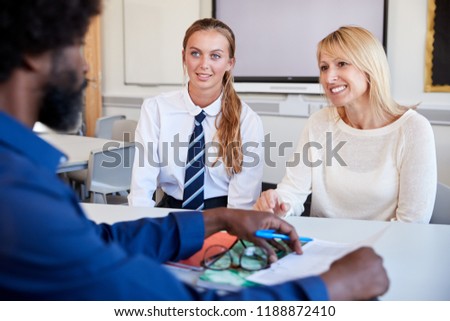 Mother And Teenage Daughter Having Discussion With Male Teacher At High School Parents Evening