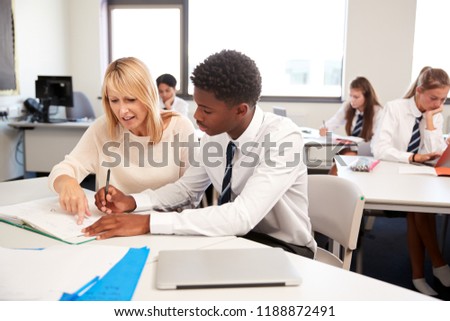 High School Tutor Giving Uniformed Male Student One To One Tuition At Desk In Classroom