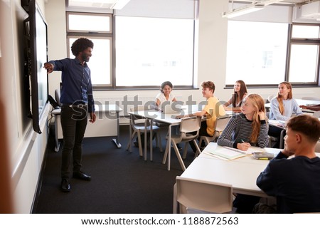 Male High School Teacher Standing Next To Interactive Whiteboard And Teaching Lesson