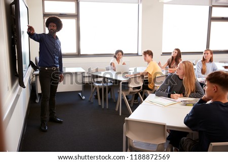 Male High School Teacher Standing Next To Interactive Whiteboard And Teaching Lesson