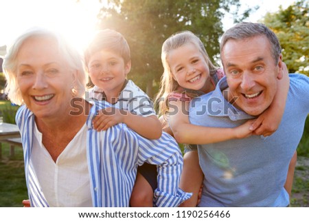 Portrait Of Smiling Grandparents Giving Grandchildren Piggyback Ride Outdoors In Summer Park