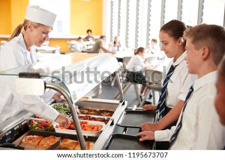 High School Students Wearing Uniform Being Served Food In Canteen