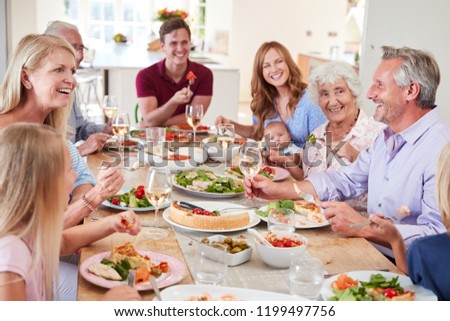 Group Of Multi-Generation Family And Friends Sitting Around Table And Making A Toast
