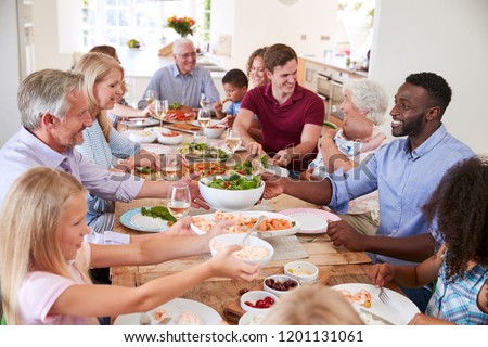 Group Of Multi-Generation Family And Friends Sitting Around Table And Enjoying Meal