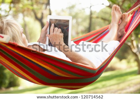 Senior Woman Relaxing In Hammock With  E-Book