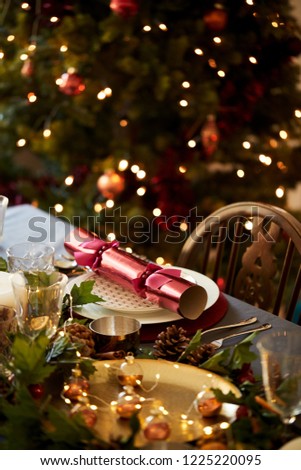 Christmas table setting a with Christmas cracker arranged on a plate and table decorations, a Christmas tree in the background