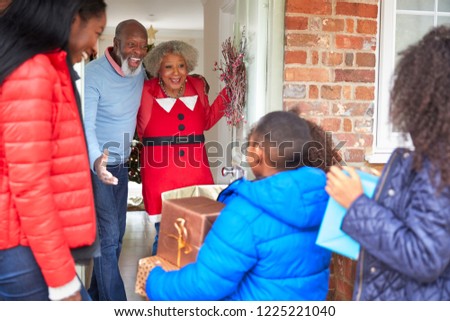 Grandparents Greeting Mother And Children As They Arrive For Visit On Christmas Day With Gifts