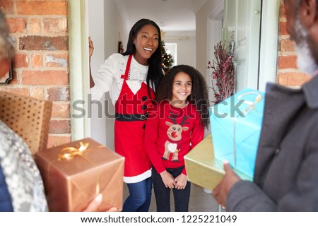 Grandparents Being Greeted By Mother And Daughter As They Arrive For Visit On Christmas Day With Gifts