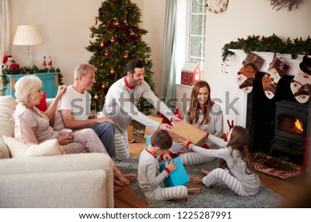 Three Generation Family Wearing Pajamas In Lounge At Home Opening Gifts On Christmas Day