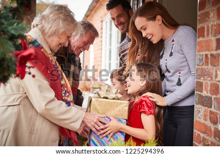 Grandparents Being Greeted By Family As They Arrive For Visit On Christmas Day With Gifts