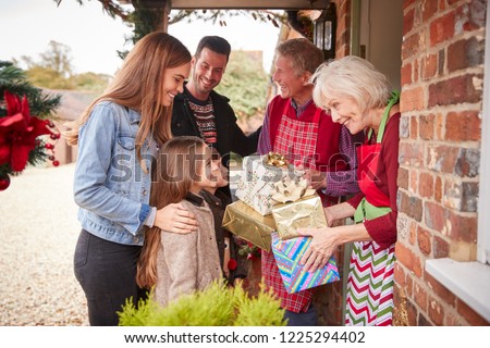 Family Being Greeted By Grandparents As They Arrive For Visit On Christmas Day With Gifts