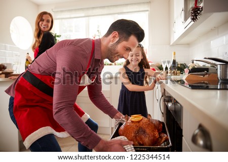 Father Getting Turkey Out Of Oven As Family Celebrate Christmas At Home Together