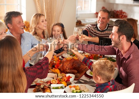 Multi-Generation Family Sitting At Table Making A Toast Whilst Eating Thanksgiving Meal At Home Together