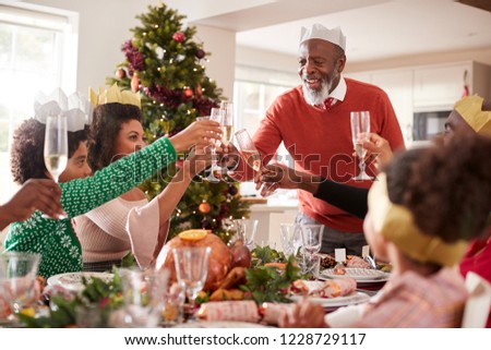 Black grandfather standing to make a toast at the head of the family Christmas dinner table, front view