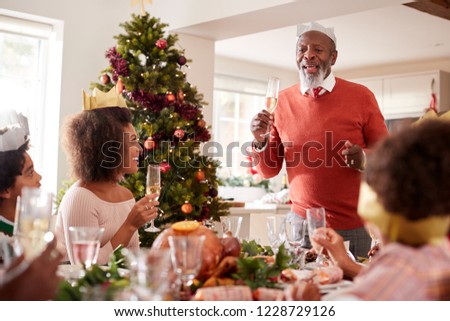 Black grandfather standing to make a speech and a toast at the head of the family Christmas dinner table, front view