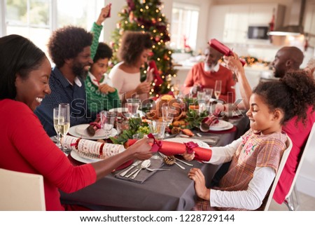Mixed race, multi generation family having fun pulling crackers at the Christmas dinner table
