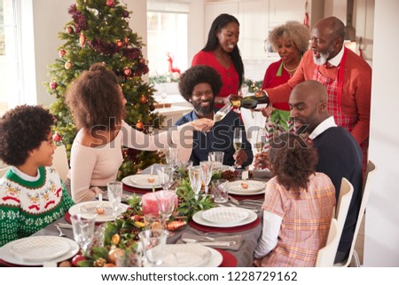 Grandfather pouring champagne at the dinner table during a multi generation, mixed race family Christmas celebration