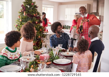Black grandfather opening champagne for his multi generation family, gathered in the dining room for Christmas dinner