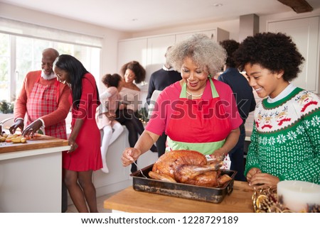 Mixed race, multi generation family gathered in kitchen before Christmas dinner, grandmother and grandson preparing roast turkey in foreground