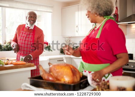 Senior black woman preparing a roast turkey for Christmas dinner turns to talk to her husband, chopping vegetables in the background, close up