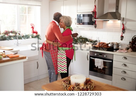 Happy mature black couple holding champagne glasses, laughing and embracing in the kitchen while preparing meal on Christmas morning, side view