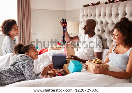 Dad sitting up in bed opening a gift on Christmas morning watched by his family, close up