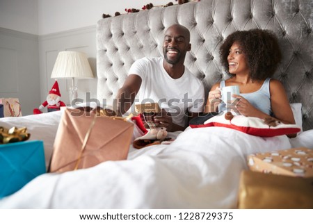 Happy young black couple sitting in bed giving gifts to each other on Christmas morning, low angle