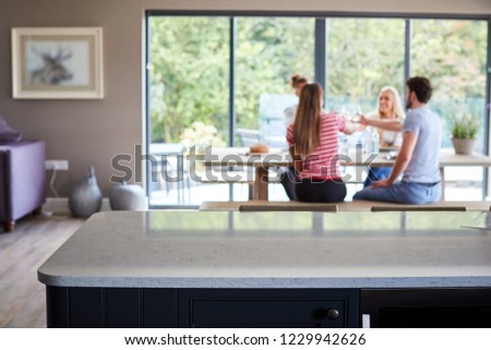 Multi ethnic group of four young adult friends celebrating at a dinner party raising their wine glasses, seen from kitchen island