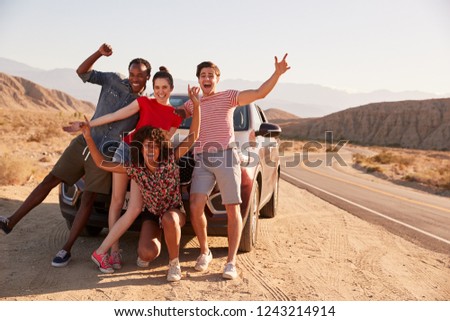 Young adult friends on road trip have fun posing by the car