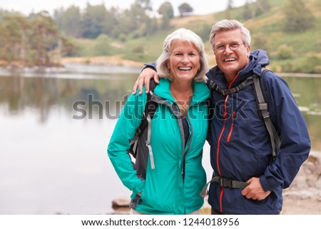 Happy senior couple standing on the shore of a lake smiling to camera, Lake District, UK