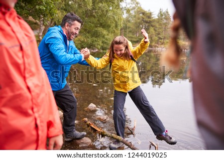 Middle aged father holding his daughterÕs hand while she balances on the shore of a lake, Lake District, UK