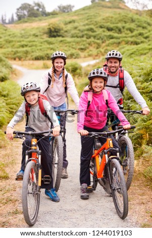 Parents and children sitting on mountain bikes in a country lane during a family camping trip, full length
