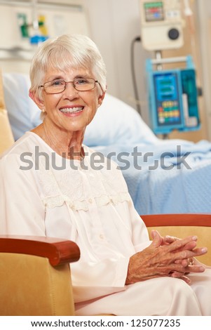 Portrait Of Senior Female Patient Seated In Chair By Hospital Bed