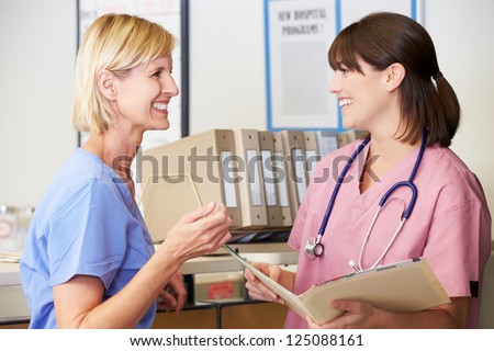 Two Nurses Discussing Patient Notes At Nurses Station