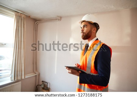 Surveyor In Hard Hat And High Visibility Jacket With Digital Tablet Carrying Out House Inspection