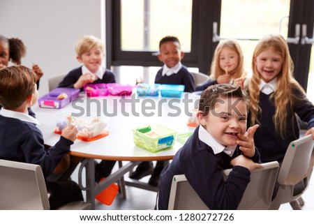 Elevated view of primary school kids sitting together at a round table to eat their packed lunches, some turning around to face the camera
